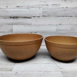 Pode incluir: Duas tigelas de cerâmica marrom de tamanhos diferentes. As tigelas são lisas e têm uma forma arredondada.