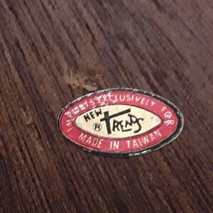 May include: A close-up of a label with the text "NEW TRENDS" in a stylized font, surrounded by a red oval border. The label also includes the text "MADE IN TAIWAN". The background is a dark wood grain.