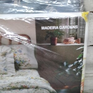 K&ouml;nnte beinhalten: Bettw&auml;sche-Set in Kunststoffverpackung. Das Set enth&auml;lt eine Bettdecke mit Blumenmuster, Kissenbez&uuml;ge und ein Kissen. Die Verpackung zeigt den Text "MADEIRA GARDENS" und eine dekorative Szene mit einer Pflanze und einer Fischstatue.