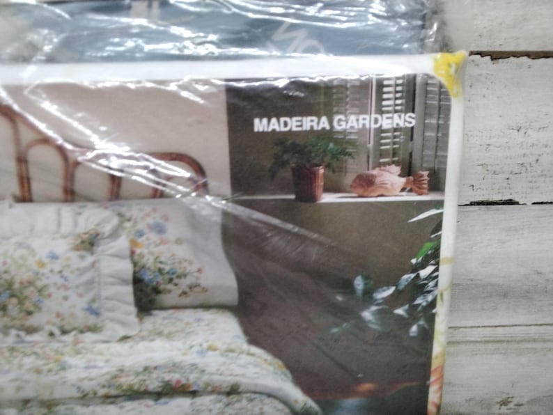 K&ouml;nnte beinhalten: Bettw&auml;sche-Set in Kunststoffverpackung. Das Set enth&auml;lt eine Bettdecke mit Blumenmuster, Kissenbez&uuml;ge und ein Kissen. Die Verpackung zeigt den Text "MADEIRA GARDENS" und eine dekorative Szene mit einer Pflanze und einer Fischstatue.