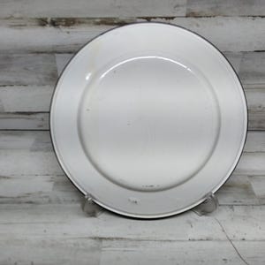 Peut inclure: Assiette en &eacute;mail blanc avec un bord noir. L'assiette est l&eacute;g&egrave;rement us&eacute;e et pr&eacute;sente quelques petites rayures.