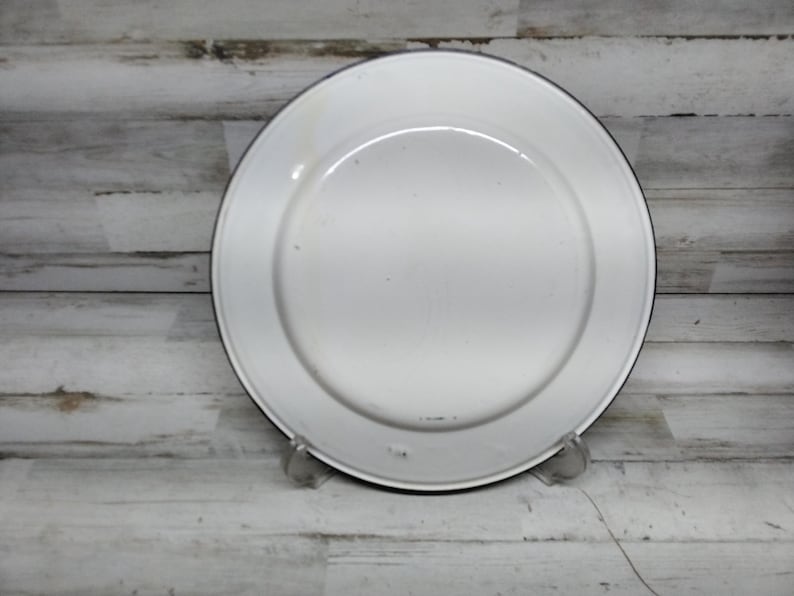 Peut inclure: Assiette en &eacute;mail blanc avec un bord noir. L'assiette est l&eacute;g&egrave;rement us&eacute;e et pr&eacute;sente quelques petites rayures.