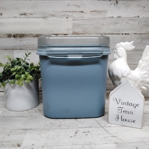 May include: A square, light blue plastic storage container with a clear, snap-on lid. Next to it sits a small white potted plant, a white ceramic rooster figurine, and a white house-shaped sign with the text Vintage Tenn House.