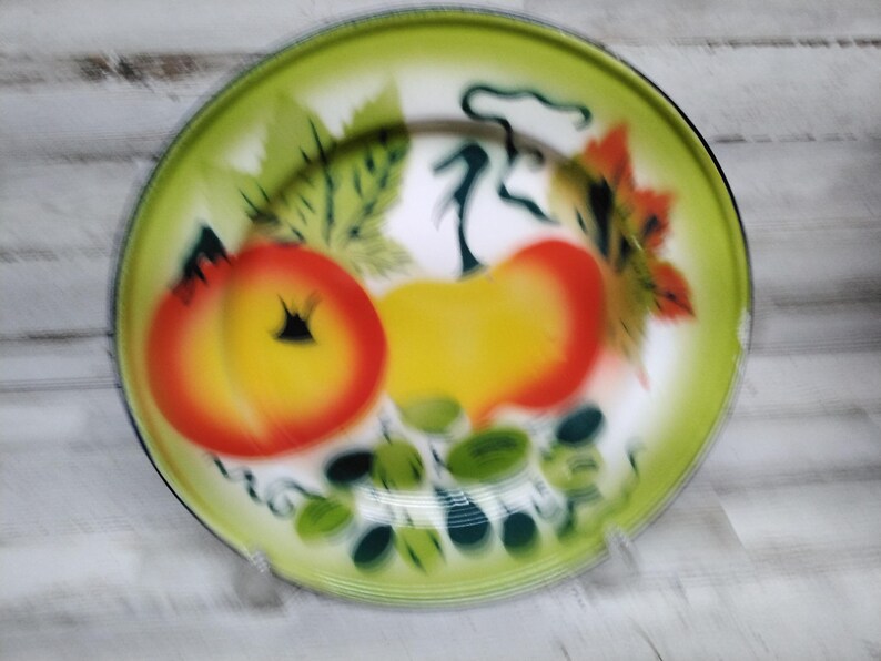 Peut inclure: Une assiette en &eacute;mail vintage avec un bord vert et un centre blanc. L'assiette pr&eacute;sente un motif peint de fruits jaunes et rouges avec des feuilles vertes.
