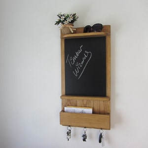 May include: A wooden wall-mounted organizer with a chalkboard, a shelf, a mail slot, and key hooks. The chalkboard has the words "Ember Wizards" written on it in white chalk.