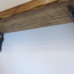 Peut inclure: Une &eacute;tag&egrave;re en bois avec deux supports en m&eacute;tal noir. L'&eacute;tag&egrave;re est en bois naturel avec une finition rustique. Les supports ont un design d&eacute;coratif.