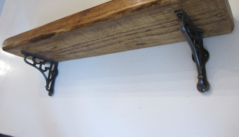 Peut inclure: Une &eacute;tag&egrave;re en bois avec deux supports en m&eacute;tal noir. L'&eacute;tag&egrave;re est en bois naturel avec une finition rustique. Les supports ont un design d&eacute;coratif.