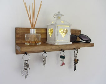 May include: A rustic wooden shelf with hooks for hanging keys, a small white lantern with heart cutouts, a glass diffuser with reeds, and sunglasses on the shelf.
