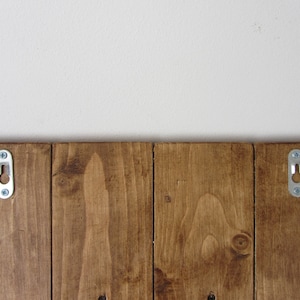 May include: A wooden sign with two metal hanging hooks on the back. The sign is stained a dark brown color.