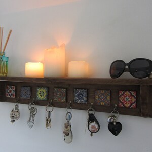 May include: A wooden key rack with colorful tile accents. The rack has seven hooks and is decorated with candles and sunglasses.