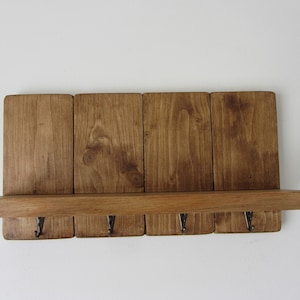 May include: A rustic wooden shelf with four hooks, stained in a dark brown color. The shelf is made of reclaimed wood and has a natural, distressed look.