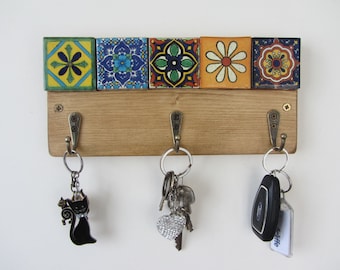 May include: A wooden key holder with three hooks. The holder is decorated with five colorful ceramic tiles featuring floral designs. There are keys hanging on two of the hooks.
