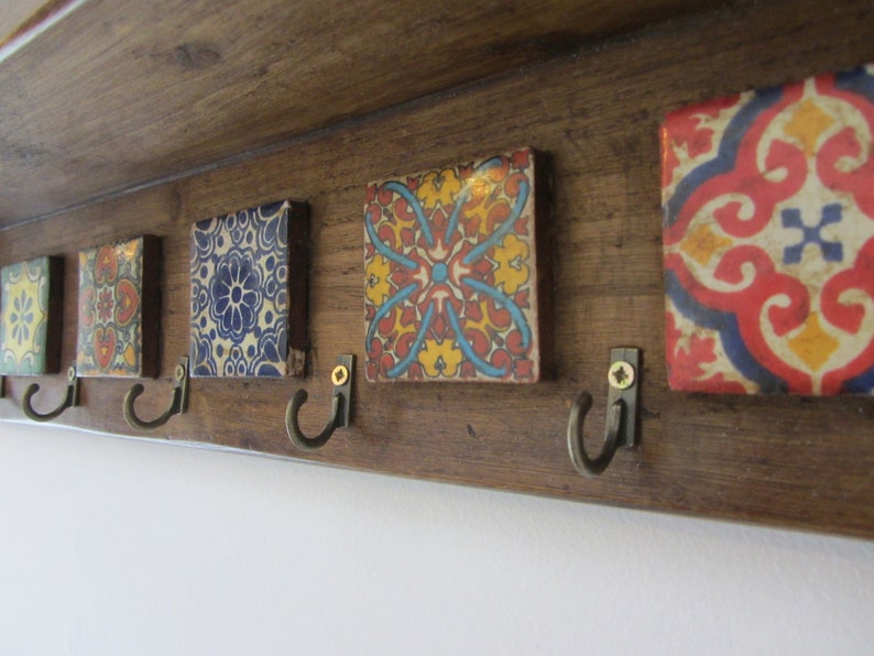 May include: A wooden coat rack with five hooks and colorful tile accents. The tiles feature intricate geometric patterns in shades of blue, red, yellow, and white.