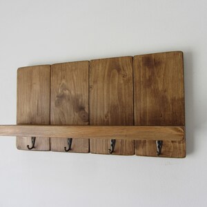 May include: A rustic wooden wall-mounted shelf with five hooks and a top shelf. The shelf is stained a dark brown color and has a natural wood grain.