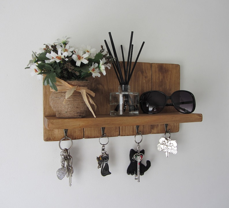 May include: Wooden key holder with five hooks, a shelf, and a small potted plant. There are sunglasses, a diffuser, and keys hanging on the hooks.