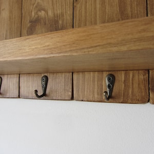 May include: A wooden wall-mounted shelf with four hooks. The shelf is stained a dark brown color and the hooks are a brushed metal finish.