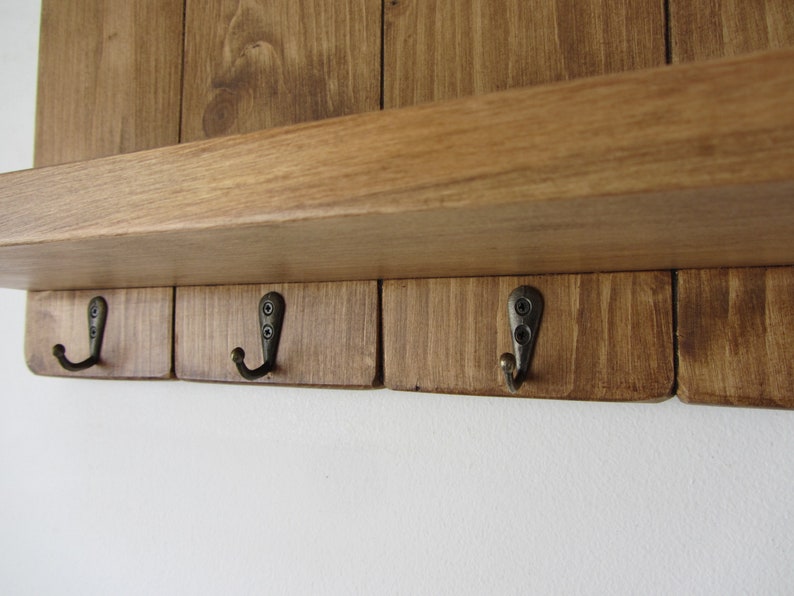 May include: A wooden wall-mounted shelf with four hooks. The shelf is stained a dark brown color and the hooks are a brushed metal finish.
