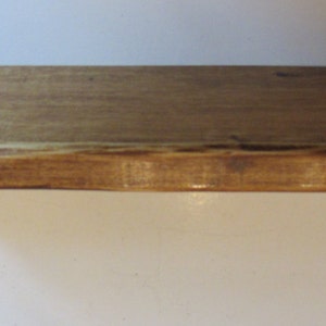 Peut inclure: Une &eacute;tag&egrave;re en bois rustique avec un bord naturel et une teinte brun fonc&eacute;. L'&eacute;tag&egrave;re est soutenue par deux supports m&eacute;talliques.