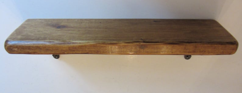 Peut inclure: Une &eacute;tag&egrave;re en bois rustique avec un bord naturel et une teinte brun fonc&eacute;. L'&eacute;tag&egrave;re est soutenue par deux supports m&eacute;talliques.