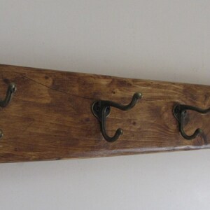 May include: A wooden wall-mounted coat rack with five hooks. The rack is stained a dark brown colour and has a rustic look.