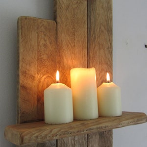 Pode incluir: Uma prateleira de parede de madeira r&uacute;stica com tr&ecirc;s velas acesas. A prateleira &eacute; feita de madeira recuperada e tem um acabamento natural e desgastado. As velas s&atilde;o brancas e est&atilde;o dispostas em fila na prateleira.
