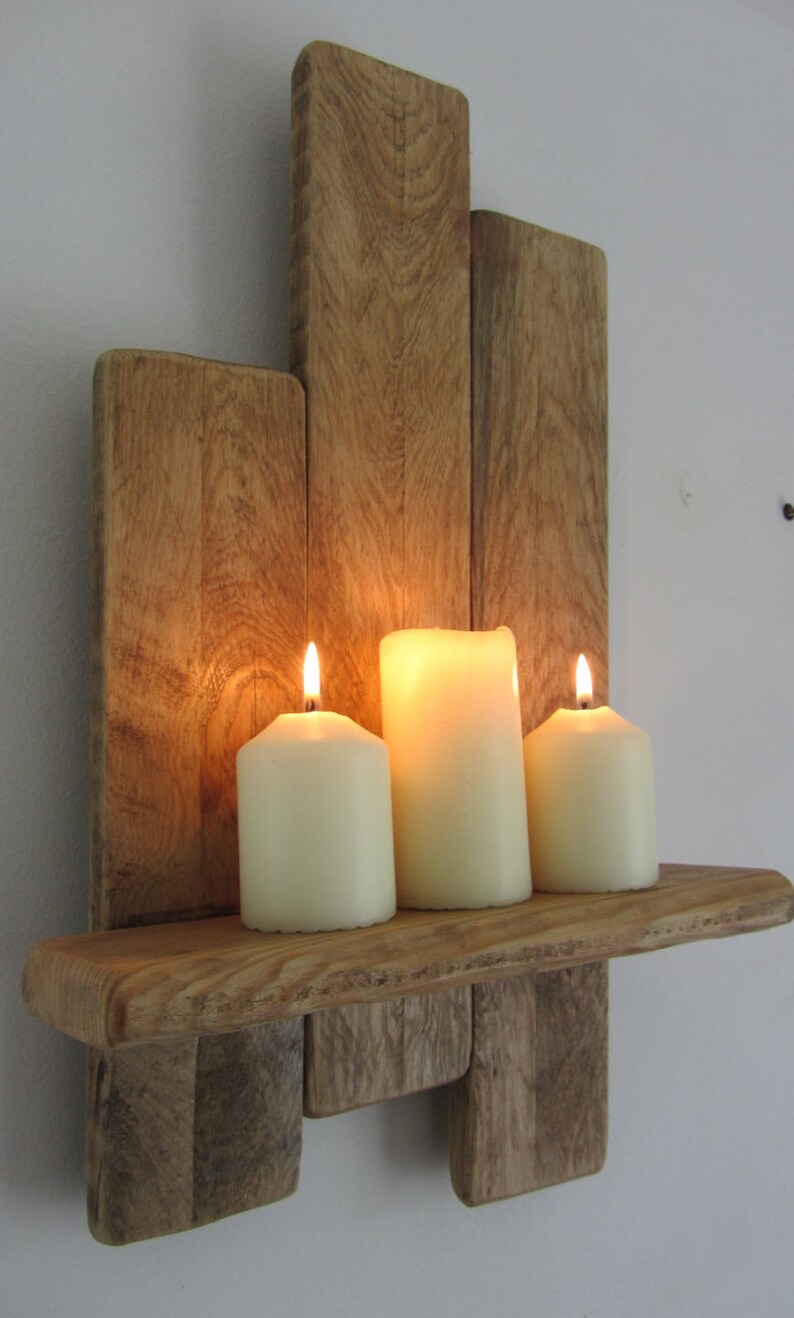 Pode incluir: Uma prateleira de parede de madeira r&uacute;stica com tr&ecirc;s velas acesas. A prateleira &eacute; feita de madeira recuperada e tem um acabamento natural e desgastado. As velas s&atilde;o brancas e est&atilde;o dispostas em fila na prateleira.