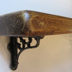 Peut inclure: Une &eacute;tag&egrave;re en bois avec une teinte brun fonc&eacute; et des supports en m&eacute;tal noir d&eacute;coratifs. L'&eacute;tag&egrave;re est fix&eacute;e &agrave; un mur blanc.