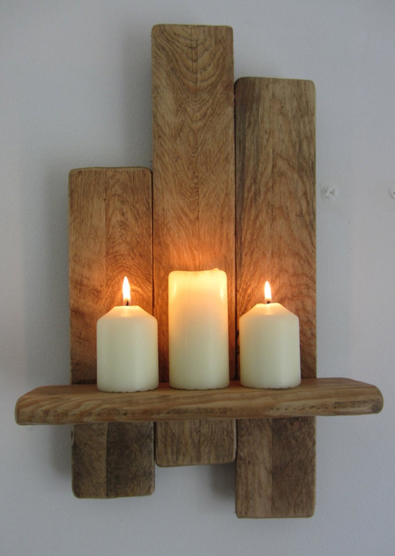Pode incluir: Uma prateleira de madeira r&uacute;stica com tr&ecirc;s velas acesas. A prateleira &eacute; feita de madeira reciclada e tem um acabamento natural. As velas s&atilde;o brancas e est&atilde;o colocadas na prateleira em fila.