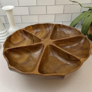 May include: A large, segmented wooden serving tray with six compartments. The tray is made of a warm-toned wood and has a natural, organic shape. It is ideal for serving snacks, appetizers, or dips at gatherings.