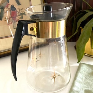 May include: Vintage glass coffee carafe with a black handle and lid, and a gold-colored band. The carafe has a clear glass body with gold starburst designs. The carafe is a mid-century modern design.