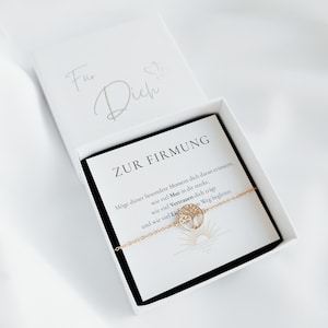 Könnte beinhalten: Ein goldfarbenes Kettenarmband mit einem runden Lebensbaum-Anhänger in einer weißen Geschenkbox. Der Deckel ist mit "Für Dich" beschriftet, während die Einlegekarte den Text "ZUR FIRMUNG", einen deutschen Spruch sowie eine stilisierte Sonnengrafik zeigt.
