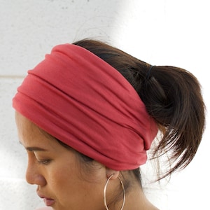 May include: A woman wearing a red headband with a silver hoop earring. She is wearing a light pink shirt.