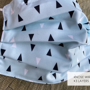 May include: A light blue face mask with a white and black triangle pattern. The mask has a nose wire and is made with 3 layers.