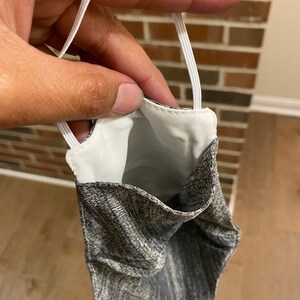 May include: A gray and white patterned face mask with white elastic ear loops. The mask is turned inside out, showing the white lining.