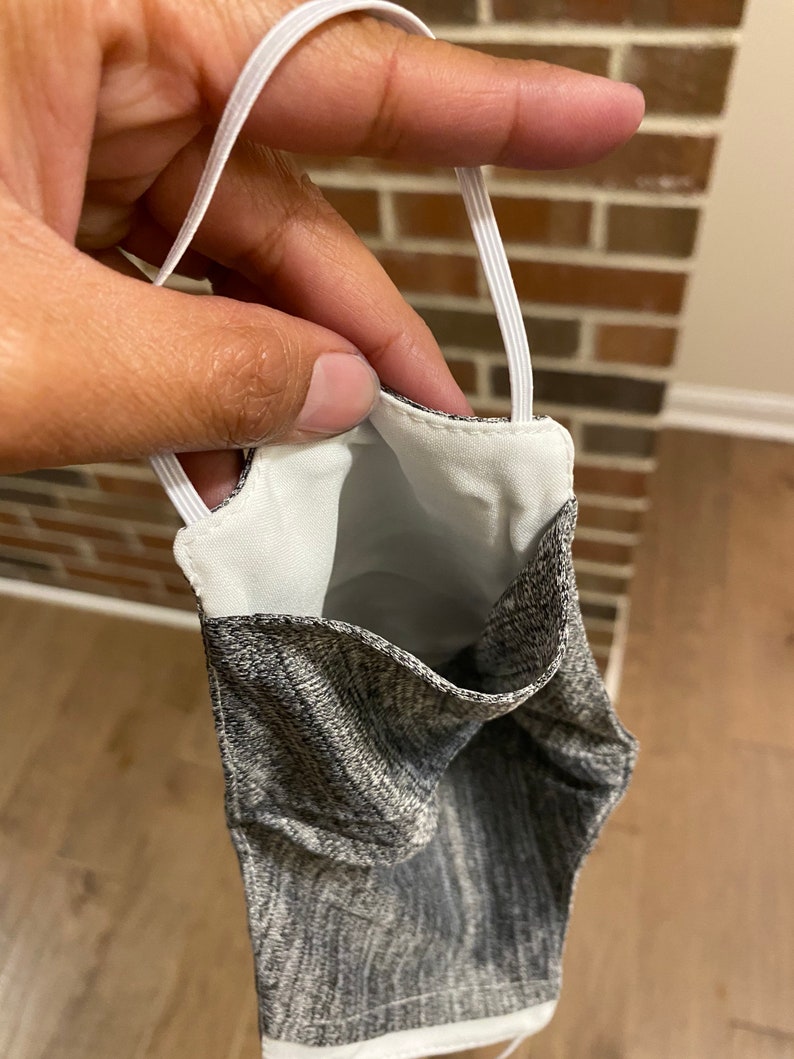 May include: A gray and white patterned face mask with white elastic ear loops. The mask is turned inside out, showing the white lining.