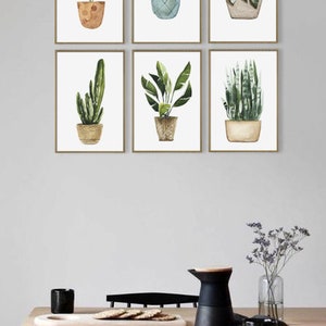 May include: A set of six watercolor prints featuring different potted plants. The prints are framed in a simple gold frame and are arranged in a grid pattern on a white wall.
