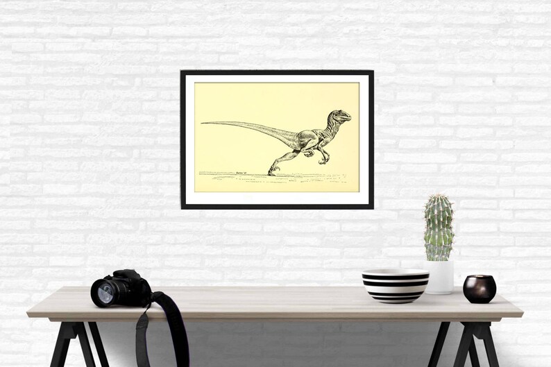 Pu&ograve; includere: Disegno in bianco e nero di un dinosauro che corre, incorniciato in una cornice nera con un passepartout color crema. Lo sfondo &egrave; un muro di mattoni bianchi.
