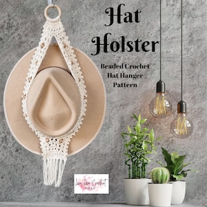 May include: A white crocheted hat hanger with beads and tassels. The hanger is hanging on a wall with a hat on it. The text "Hat Holster Beaded Crochet Hat Hanger Pattern Live Love Crochet SHAZ" is visible in the image.