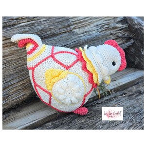 Peut inclure: Un poulet au crochet fait à la main, blanc, rose et jaune. Le poulet présente un design détaillé avec une fleur sur le côté et une crête rouge. Le travail au crochet est visible, mettant en valeur la texture et le savoir-faire.