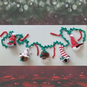 Op de afbeelding: Een kerstkrans met gehaakte dierenversieringen. De krans is gemaakt van groen en rood garen en heeft een koala, een pinguïn, een rendier en een gnome. Elk ornament draagt ​​een feestelijke hoed.