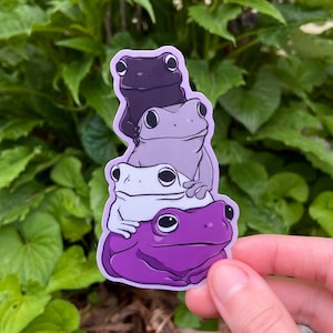 Könnte beinhalten: Ein gestanzter Aufkleber mit einem vertikalen Stapel aus vier Fröschen in einem Farbverlauf aus Violetttönen, der von einem dunklen Violett oben bis zu einem leuchtenden Violett an der Basis reicht, mit großen schwarzen Augen und glatter Haut.