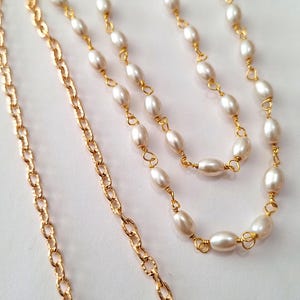 May include: A layered necklace featuring white oval pearls strung on gold wire, paired with a textured gold chain. The jewelry is displayed against a white background, showcasing the contrast of colors and textures.