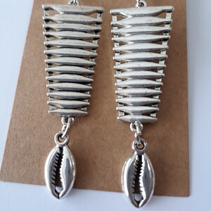 May include: Silver dangle earrings with a geometric design and a shell charm.
