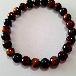 May include: A brown, black, and gold tiger's eye beaded bracelet. The bracelet is made of round beads and is strung on a clear elastic cord.