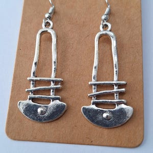 May include: A pair of silver dangle earrings with a geometric design. The earrings have a curved bottom and a straight top with a horizontal bar.