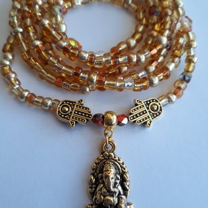 May include: A gold beaded wrap bracelet with a gold charm of the Hindu deity Ganesha. The bracelet is made with small, round beads in shades of gold and amber.