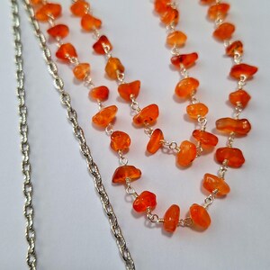 May include: A silver chain necklace with a double strand of orange carnelian beads. The beads are irregular in shape and have a natural, rough texture.