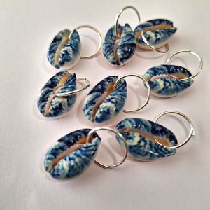 May include: Eight blue and white cowrie shell charms with silver jump rings. The shells have a natural, organic pattern.