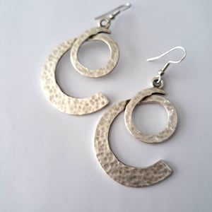May include: A pair of silver earrings with a hammered finish. Each earring features two interlocking circles, one larger than the other.