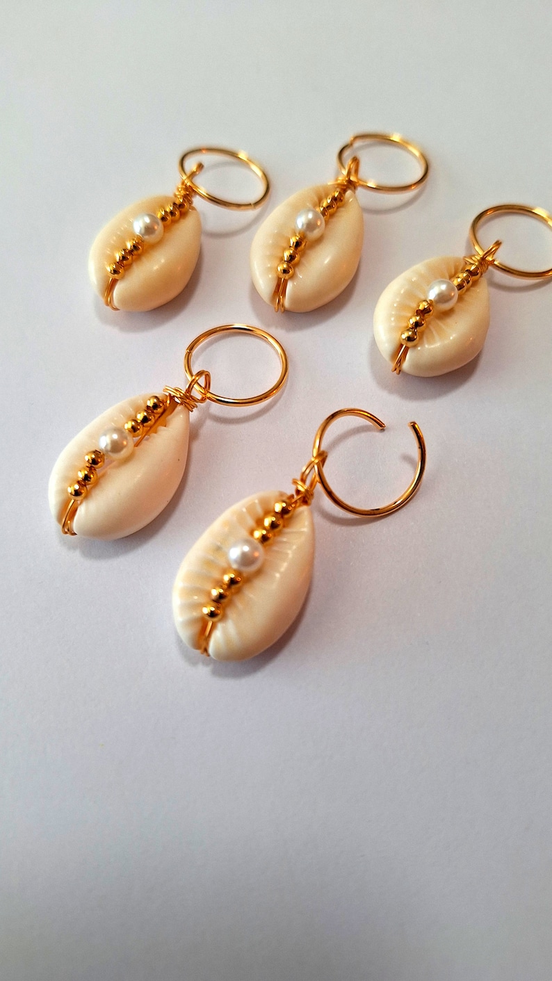 May include: Five gold hair clips with white seashells and pearl accents. Each clip features a small, white seashell with a single pearl bead in the centre, surrounded by gold beads.